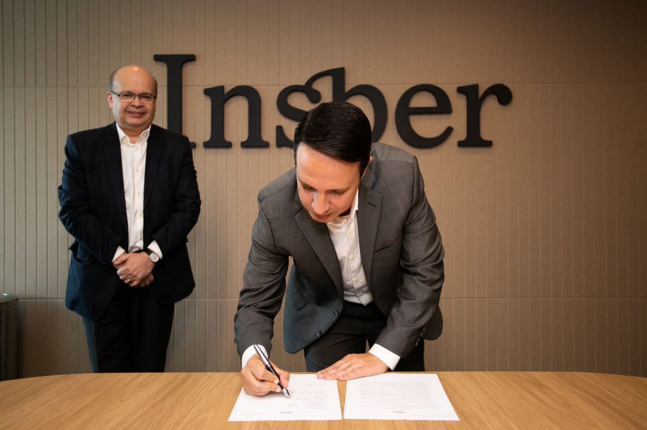Guilherme Martins signs the agreement, observed by Paulo Cunha.
